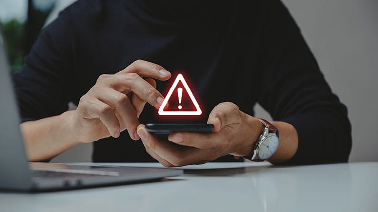 Graphic showing an alert symbol overlaid on the picture of a person holding a phone. 